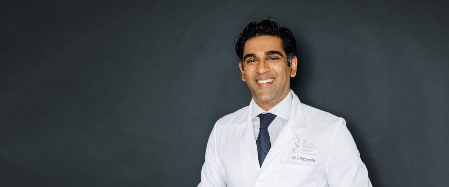 Smiling doctor in a lab coat against backdrop.